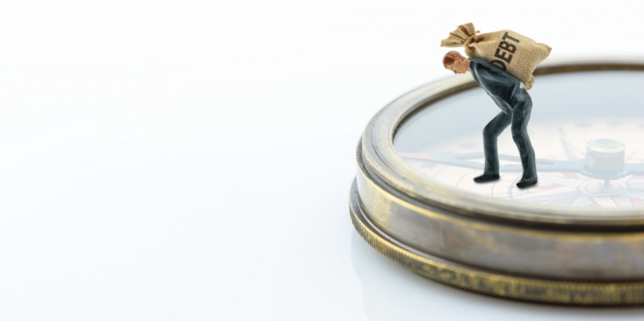 a tiny figurine holds a bag of debt, standing atop a compass